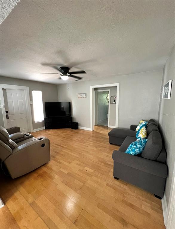 A living room features light wood flooring, a gray sectional sofa, and a ceiling fan — 3910 E ELLICOTT STREET, TAMPA, FL