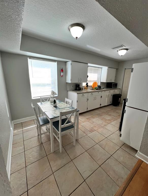 A kitchen with white cabinets, tile flooring, and a small dining table near a window — 3910 E ELLICOTT STREET, TAMPA, FL