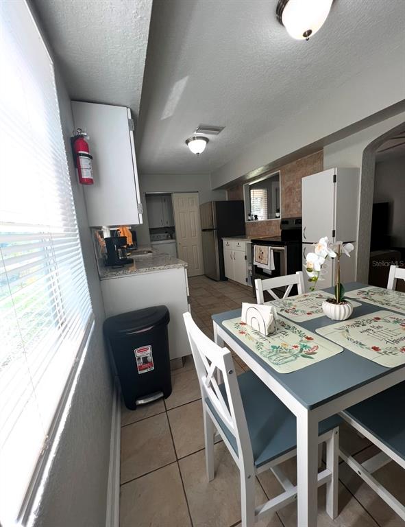 A kitchen features white cabinets, stainless steel appliances, a dining table, and tile flooring — 3910 E ELLICOTT STREET, TAMPA, FL