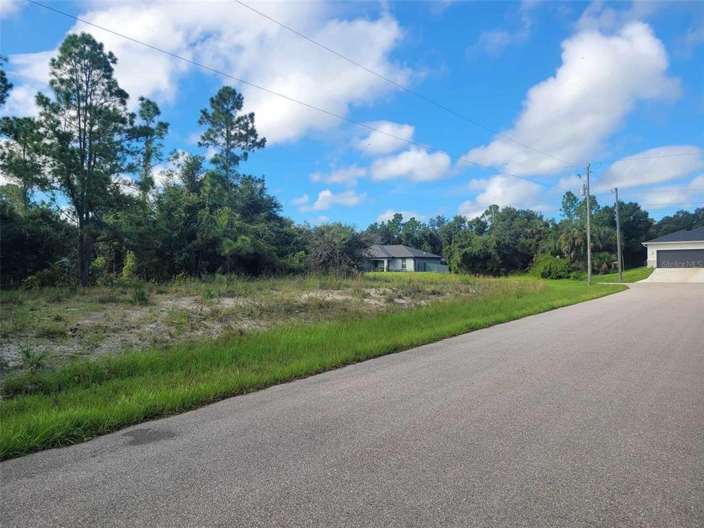 A vacant, grassy residential lot sits next to a paved road with trees in the background — SCENIC ROAD, NORTH PORT, FL