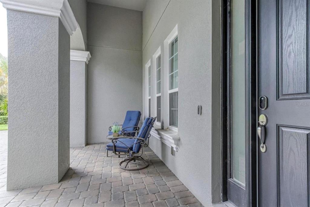 A covered porch features stone pavers, two blue chairs, and a dark front door — 7573 GREEN MOUNTAIN WAY, WINTER GARDEN, FL