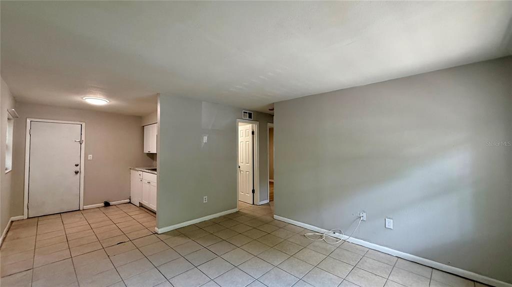 A room with light-colored tile flooring, gray walls, a white door, and a small kitchen area — 409 LAKE STREET, WILDWOOD, FL
