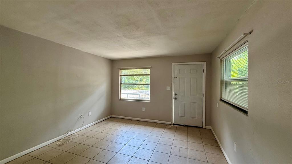 An empty room with light-colored walls, tiled flooring, two windows, and a white entry door — 409 LAKE STREET, WILDWOOD, FL
