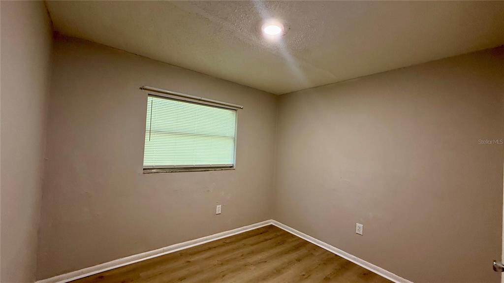 An empty bedroom features beige walls, a single window with blinds, and wood-look flooring — 409 LAKE STREET, WILDWOOD, FL