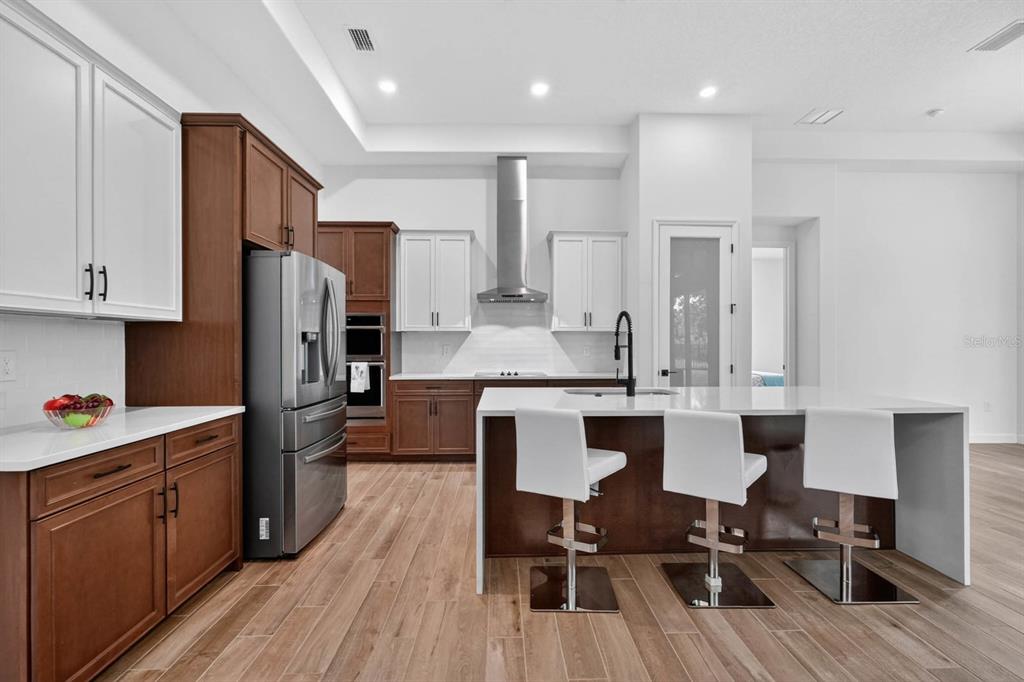 A modern kitchen features two-toned cabinetry, a large island with bar seating, and stainless steel appliances — 46 NEW LEATHERWOOD DRIVE, PALM COAST, FL