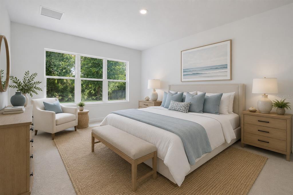 A bright, staged bedroom features a king bed, neutral decor, and large windows overlooking trees — 46 NEW LEATHERWOOD DRIVE, PALM COAST, FL