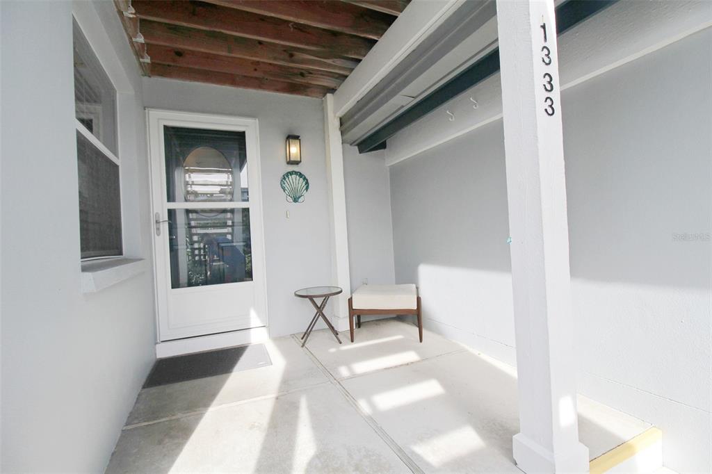 A covered concrete porch features a white front door, a small table, and a stool — 1333 SIESTA BAYSIDE DRIVE UNIT 1333-D, SARASOTA, FL