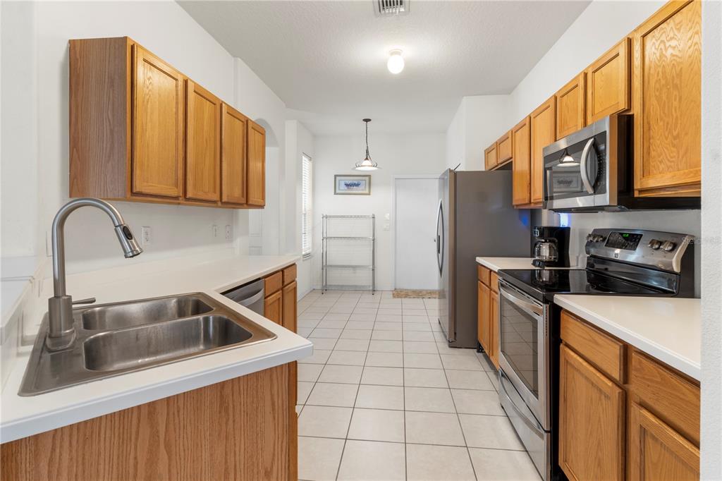 A galley kitchen features oak cabinets, white countertops, stainless steel appliances, and light tile flooring — 8316 106TH AVENUE, VERO BEACH, FL