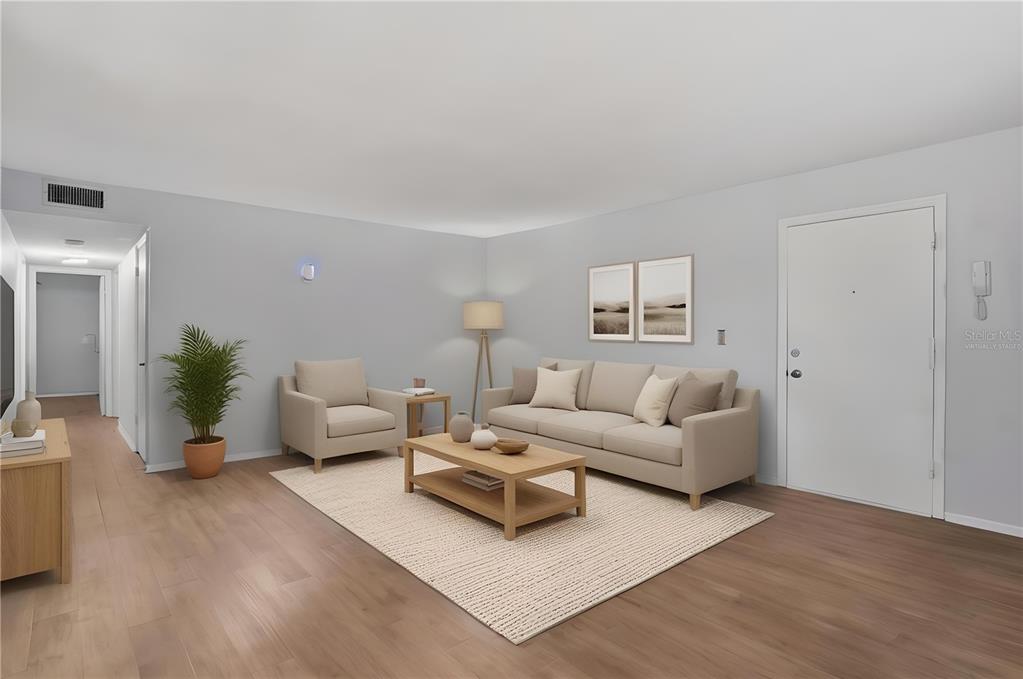 This virtually staged living room features light wood flooring, a beige sofa, and an armchair — 1715 BELLEAIR FOREST DRIVE UNIT A, BELLEAIR, FL