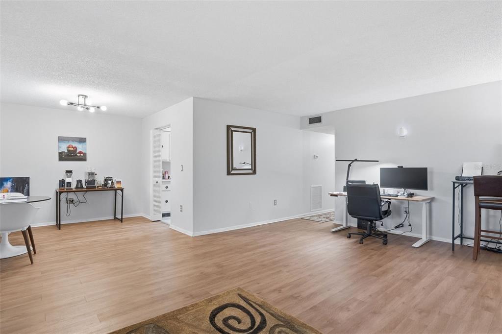 A spacious room with light wood-look flooring, a home office area, and a coffee station — 1715 BELLEAIR FOREST DRIVE UNIT A, BELLEAIR, FL
