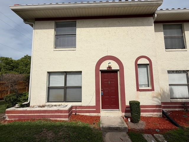 A two-story townhouse exterior features beige stucco walls, a red front door, and red trim — 1610 LITTLE RIVER DRIVE UNIT 20, ORLANDO, FL