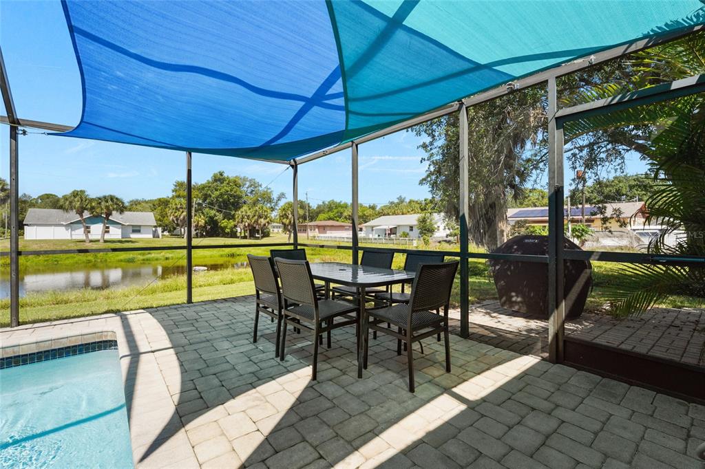 A screened-in pool patio features a dining set, a grill, and a blue shade sail — 2240 GENTIAN ROAD, VENICE, FL
