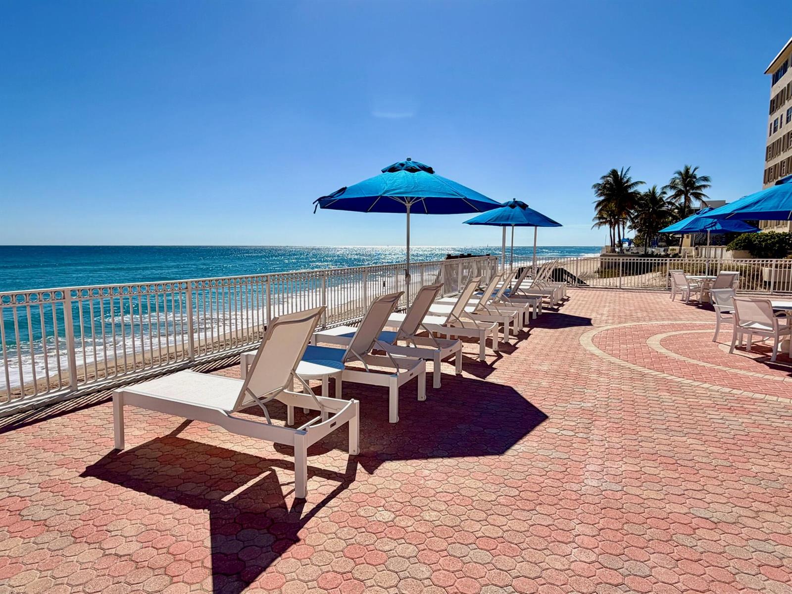 A paved pool deck features lounge chairs and blue umbrellas overlooking the ocean — 3460 S Ocean Boulevard # 2090, Palm Beach FL 33480, PALM BEACH, FL