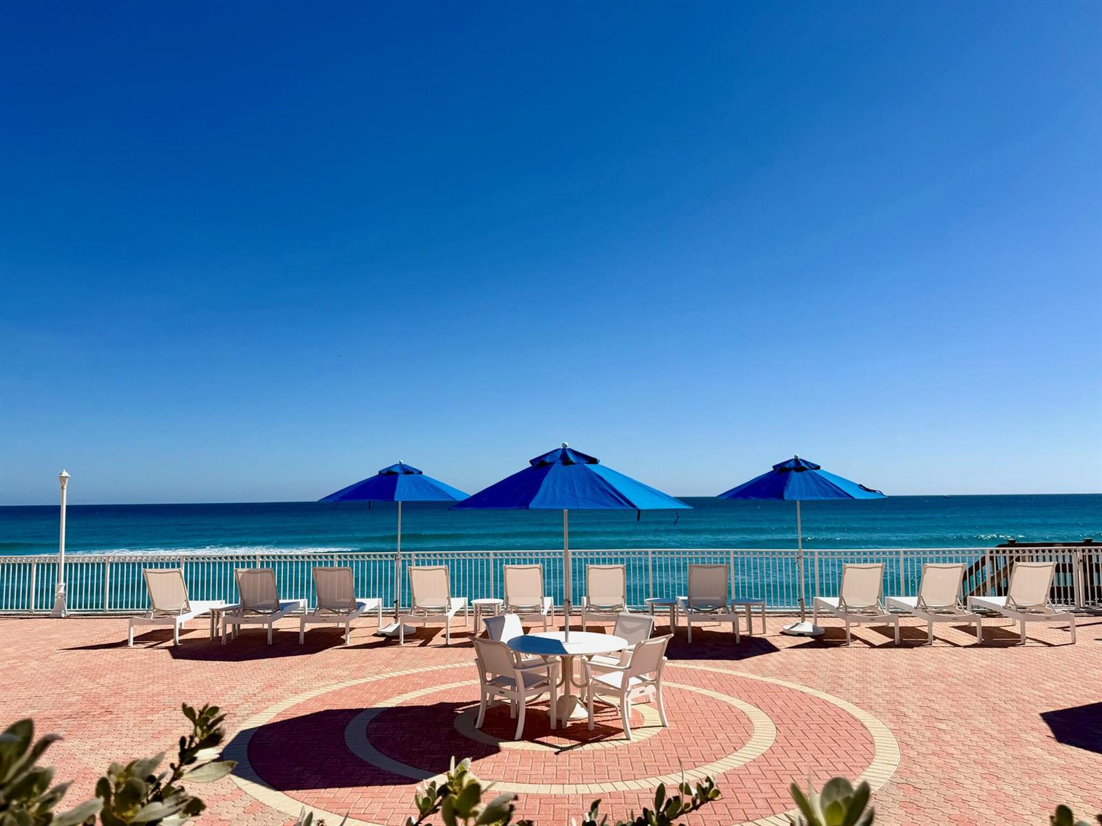 A patio with lounge chairs and umbrellas overlooks the ocean behind a white metal fence — 3460 S Ocean Boulevard # 2090, Palm Beach FL 33480, PALM BEACH, FL