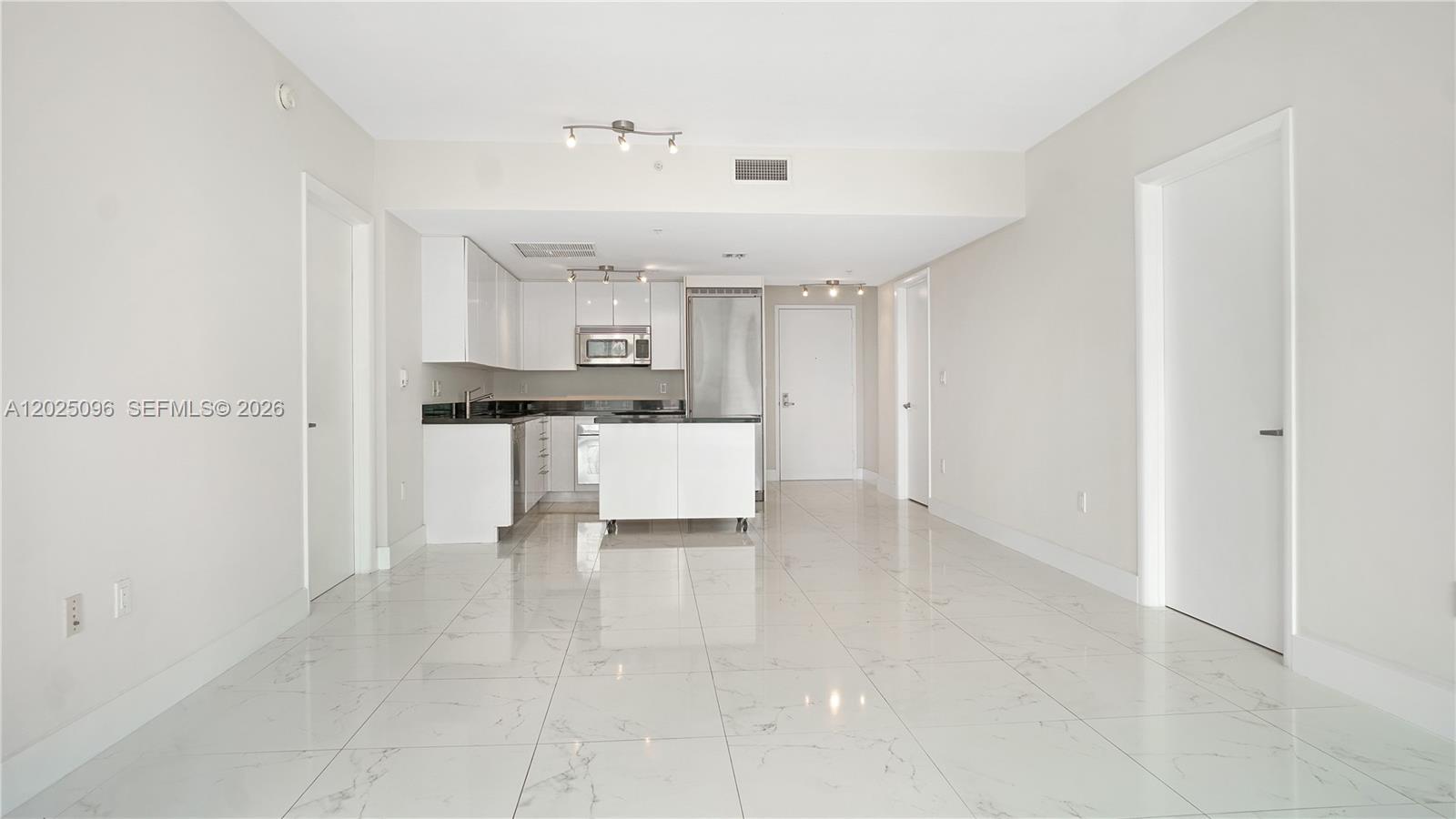 A modern kitchen with white cabinets and stainless steel appliances opens into a tiled room — 92 SW 3rd St # 1803, Miami FL 33130, MIAMI, FL