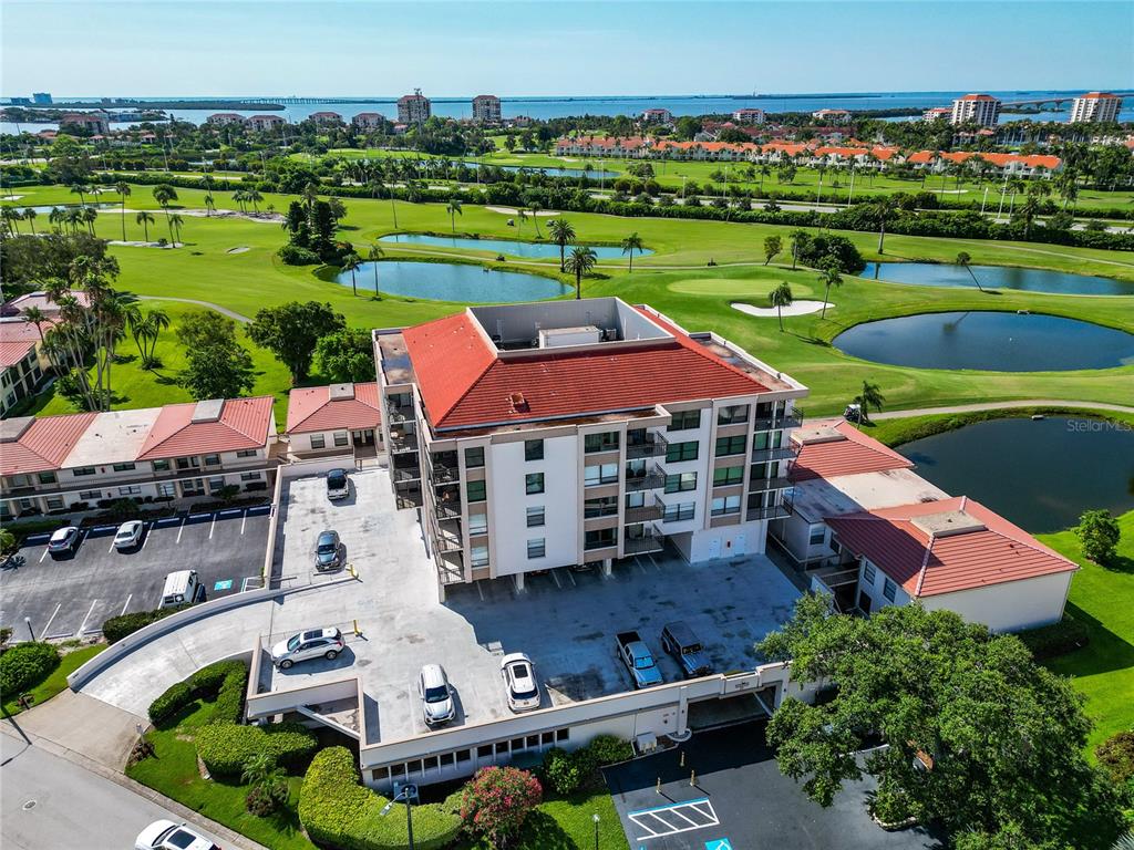 An aerial view shows a multi-story apartment building with a red roof and parking lot — 6210 SUN BOULEVARD UNIT 506, ST PETERSBURG, FL