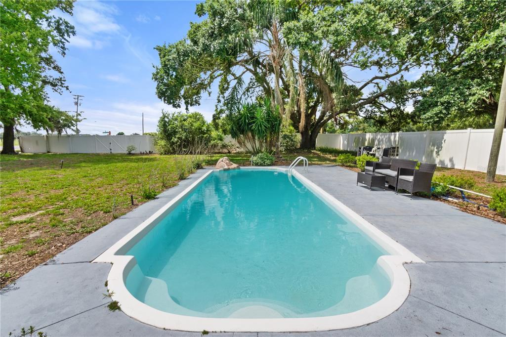 An outdoor swimming pool with a concrete deck and patio furniture in a grassy backyard — 245 ALTURAS ROAD, BARTOW, FL