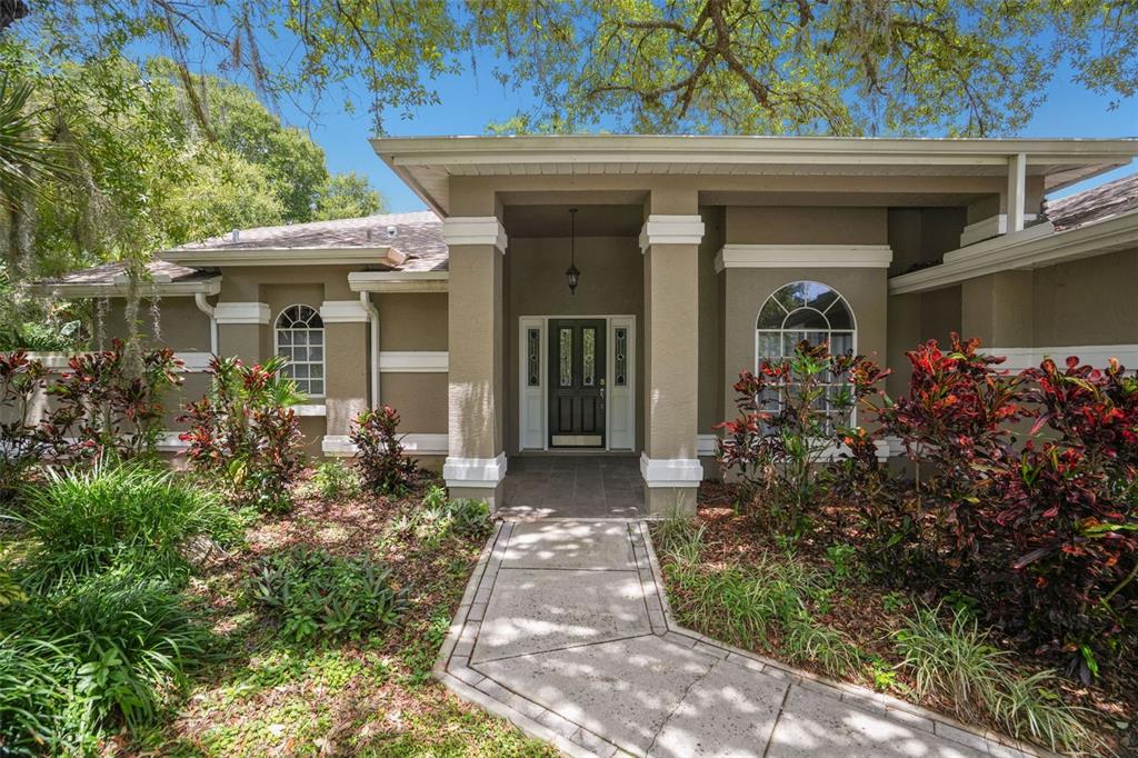 A tan single-story house with a covered entryway, arched windows, and a paved walkway — 8020 MOONLIGHT LANE, NEW PORT RICHEY, FL