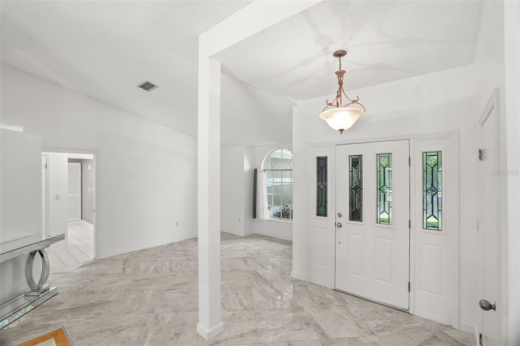 A bright entryway features white walls, marble-look tile flooring, and a decorative glass-paneled front door — 8020 MOONLIGHT LANE, NEW PORT RICHEY, FL