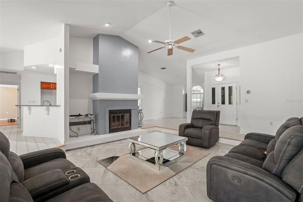 A living room features a gray fireplace, tiled floors, a ceiling fan, and gray furniture — 8020 MOONLIGHT LANE, NEW PORT RICHEY, FL