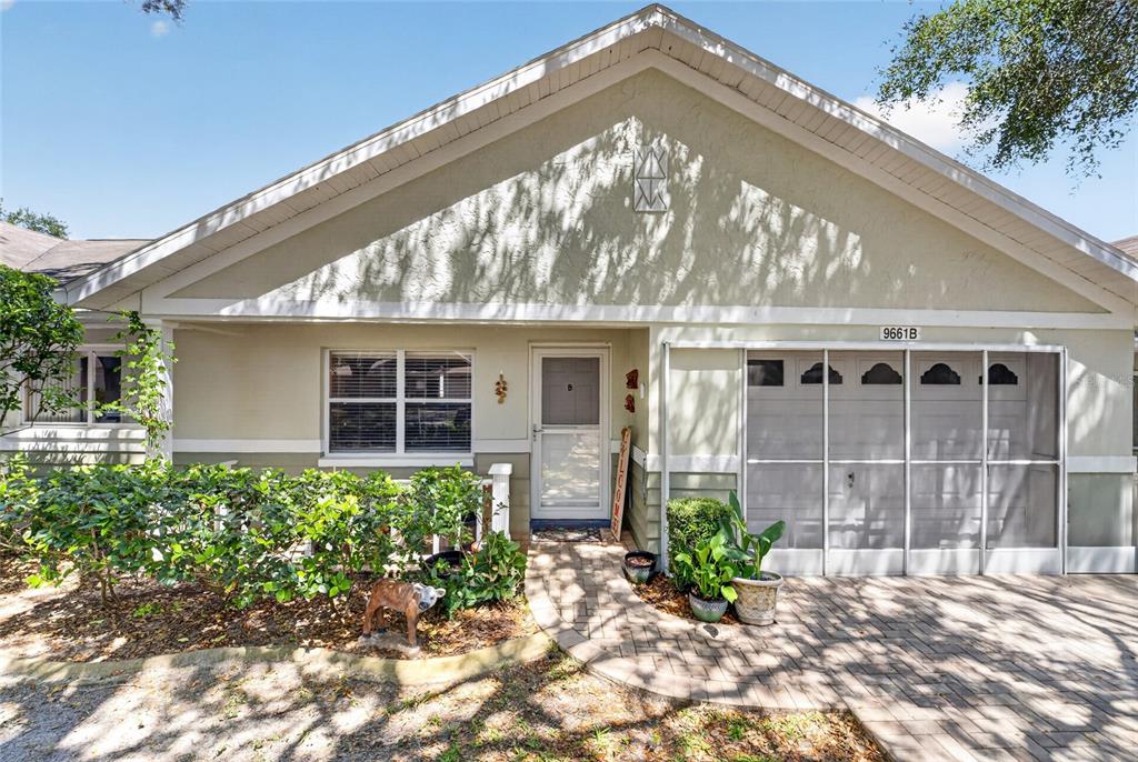The exterior of a single-story home features a paved walkway, a screened garage, and landscaping — 9661 SW 95TH COURT UNIT B, OCALA, FL