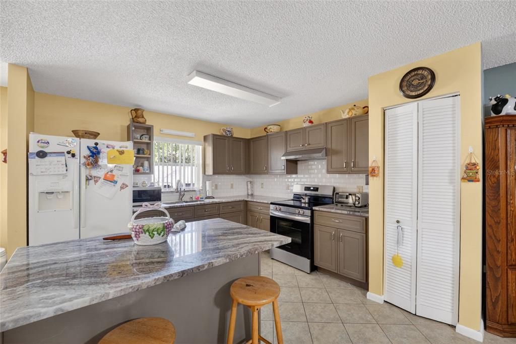 A kitchen features gray cabinets, a granite-topped island with stools, and white appliances — 9661 SW 95TH COURT UNIT B, OCALA, FL