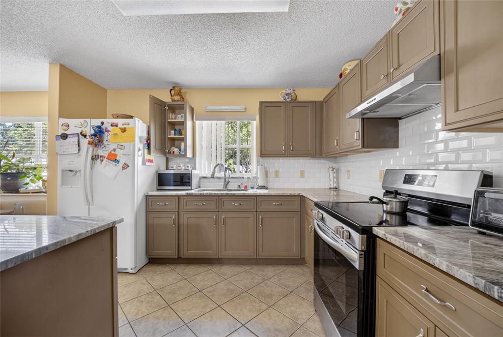 A kitchen features brown cabinets, granite countertops, white subway tile backsplash, and stainless steel appliances — 9661 SW 95TH COURT UNIT B, OCALA, FL