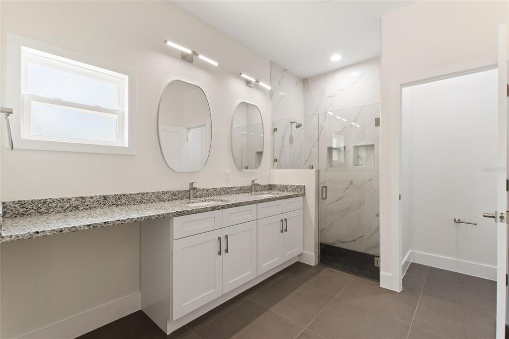 A modern bathroom features a double vanity with granite countertops, white cabinets, and a glass-enclosed shower — 3970 LAGUNA DRIVE, INDIAN LAKE ESTATES, FL