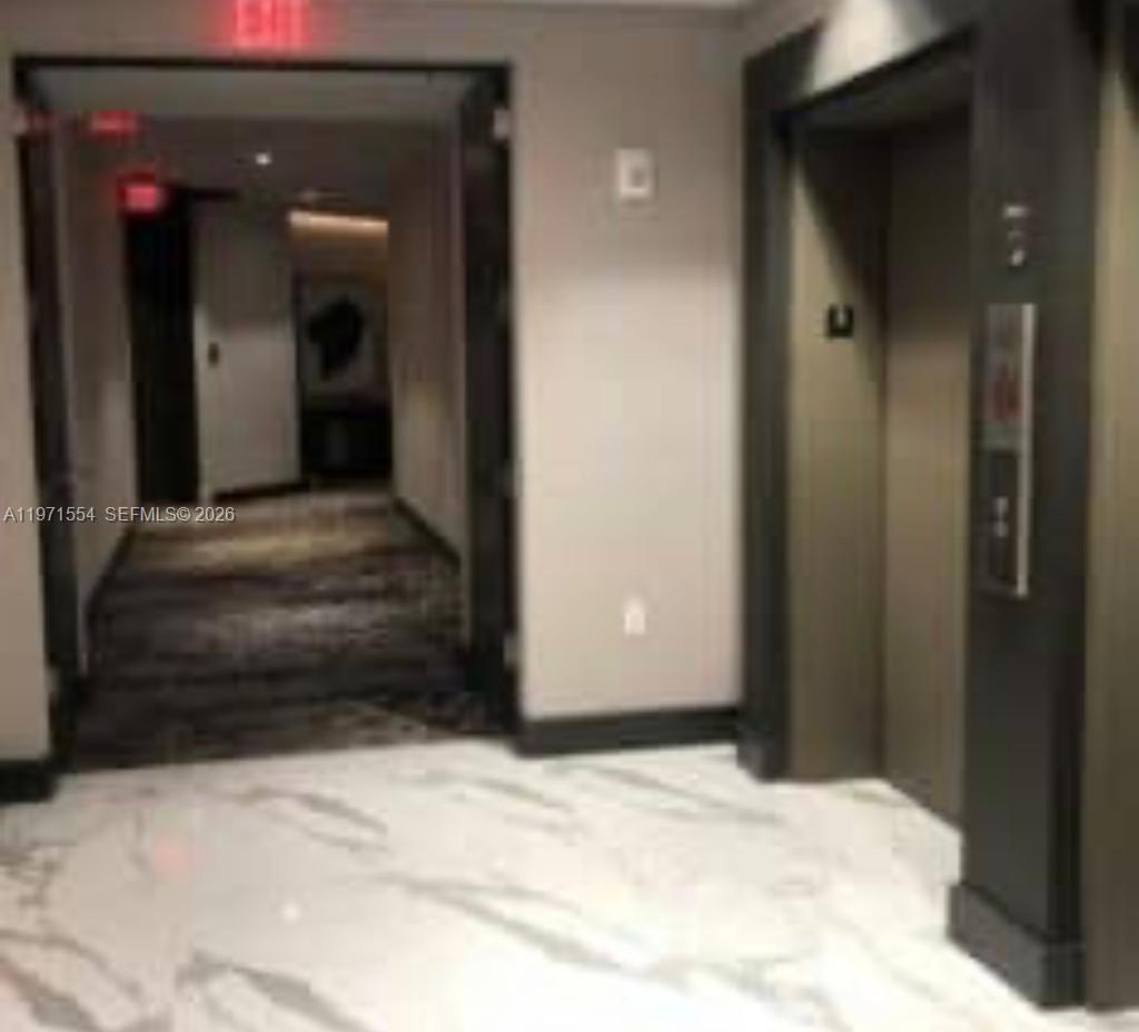 A hallway with marble flooring leads to an elevator and a doorway with an exit sign — 301 Altara Ave # 805, Coral Gables FL 33146, CORAL GABLES, FL