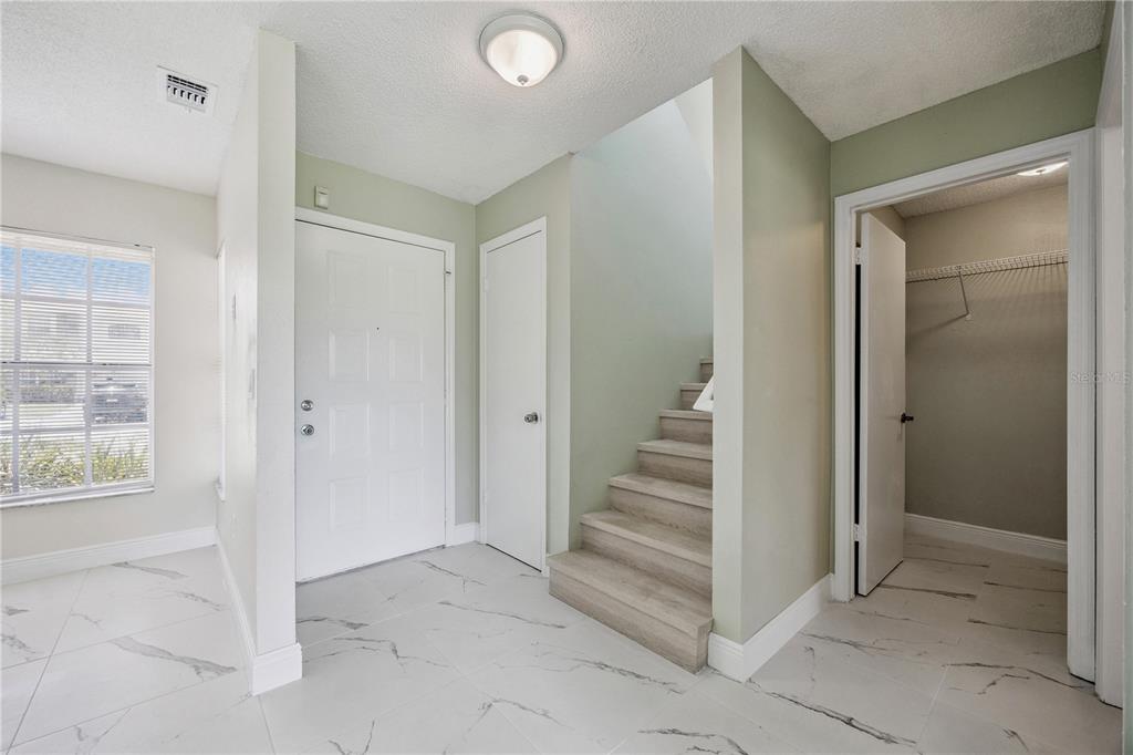 An entryway features white marble-look tile flooring, a staircase with wood treads, and a closet — 14451 BAY ISLE DRIVE, ORLANDO, FL