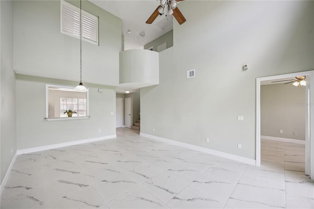 A spacious living room with high ceilings, white marble-look tile flooring, and a pass-through window — 14451 BAY ISLE DRIVE, ORLANDO, FL