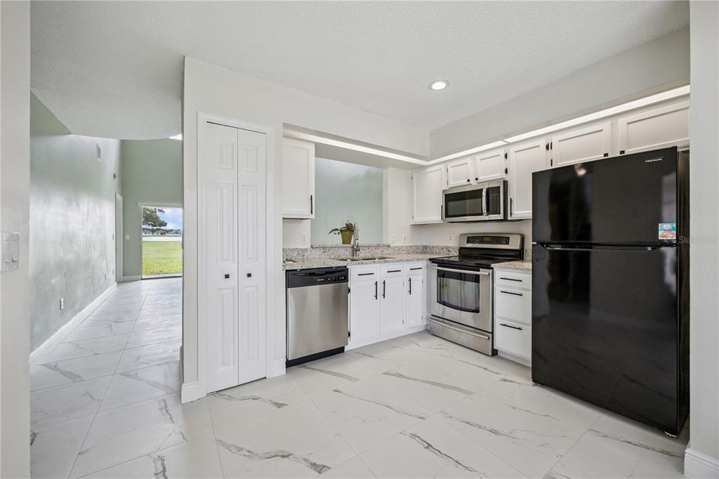 A kitchen features white cabinets, stainless steel appliances, a black refrigerator, and marble-patterned tile flooring — 14451 BAY ISLE DRIVE, ORLANDO, FL