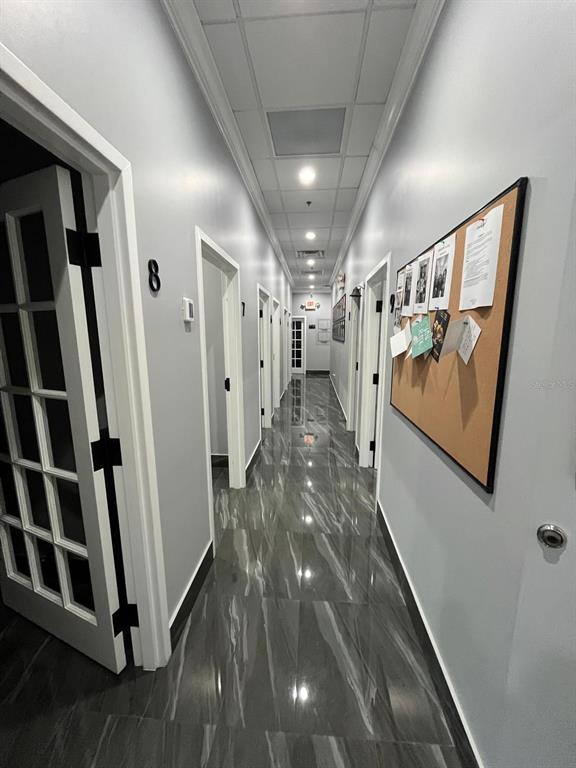 A long hallway features gray walls, dark marble-patterned tile flooring, and a cork bulletin board — 7901 KINGSPOINTE PARKWAY UNIT 19 # Office 4, ORLANDO, FL