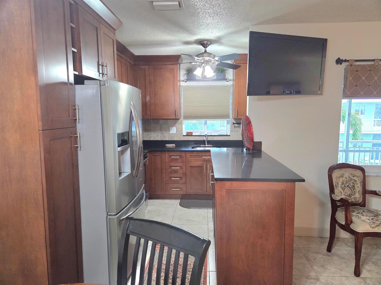 A kitchen features wood cabinets, stainless steel appliances, a black countertop, and a ceiling fan — 2100 NE 38th Street NE # 207, Lighthouse Point FL 33064, LIGHTHOUSE POINT, FL