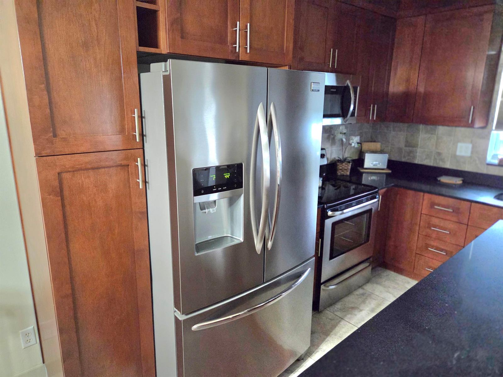 A kitchen features stainless steel appliances, dark wood cabinetry, and black countertops — 2100 NE 38th Street NE # 207, Lighthouse Point FL 33064, LIGHTHOUSE POINT, FL