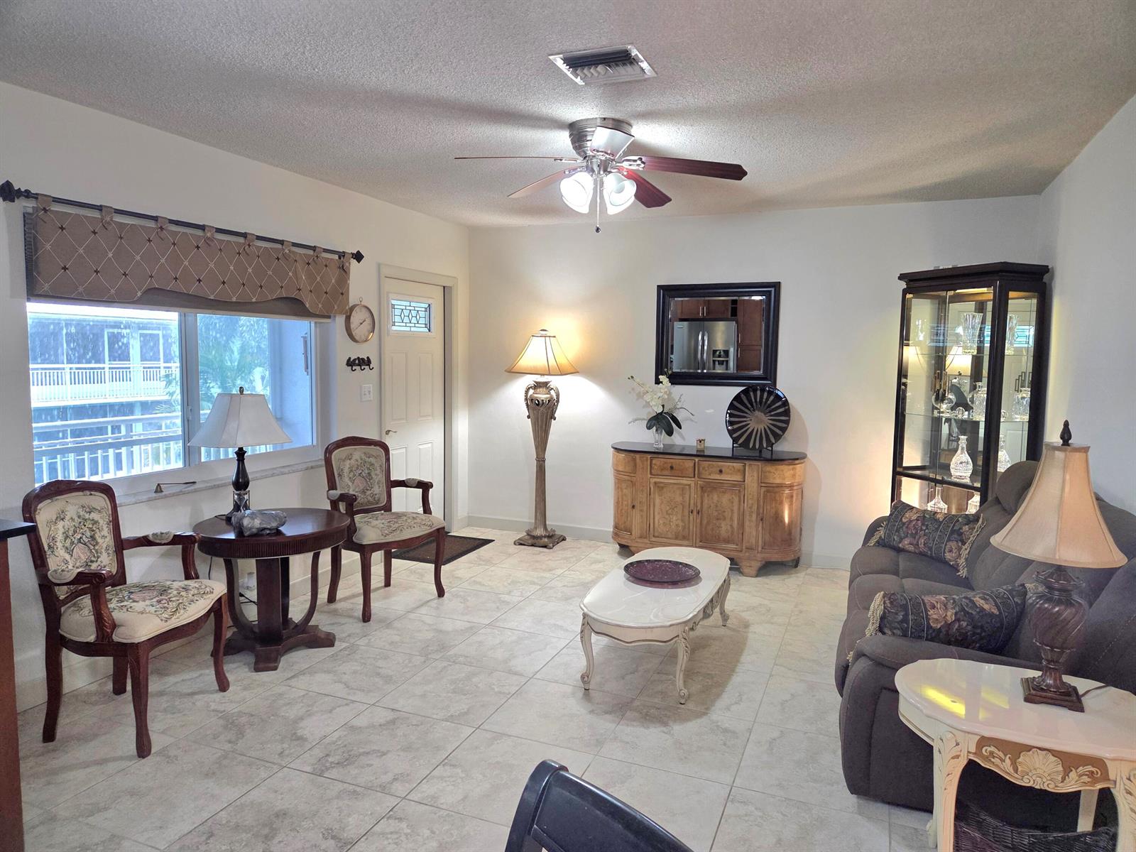 A living room features tile flooring, a ceiling fan, a glass display cabinet, and furniture — 2100 NE 38th Street NE # 207, Lighthouse Point FL 33064, LIGHTHOUSE POINT, FL