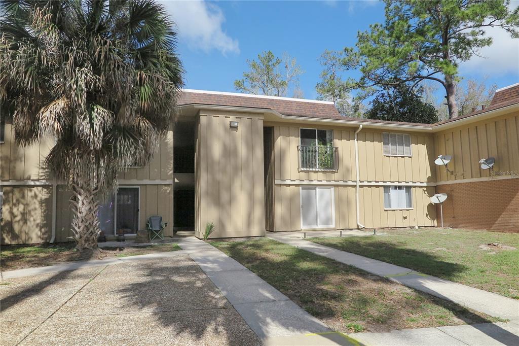 A two-story tan apartment building with vertical siding and a palm tree in the foreground — 507 NW 39TH DRIVE UNIT 210, GAINESVILLE, FL