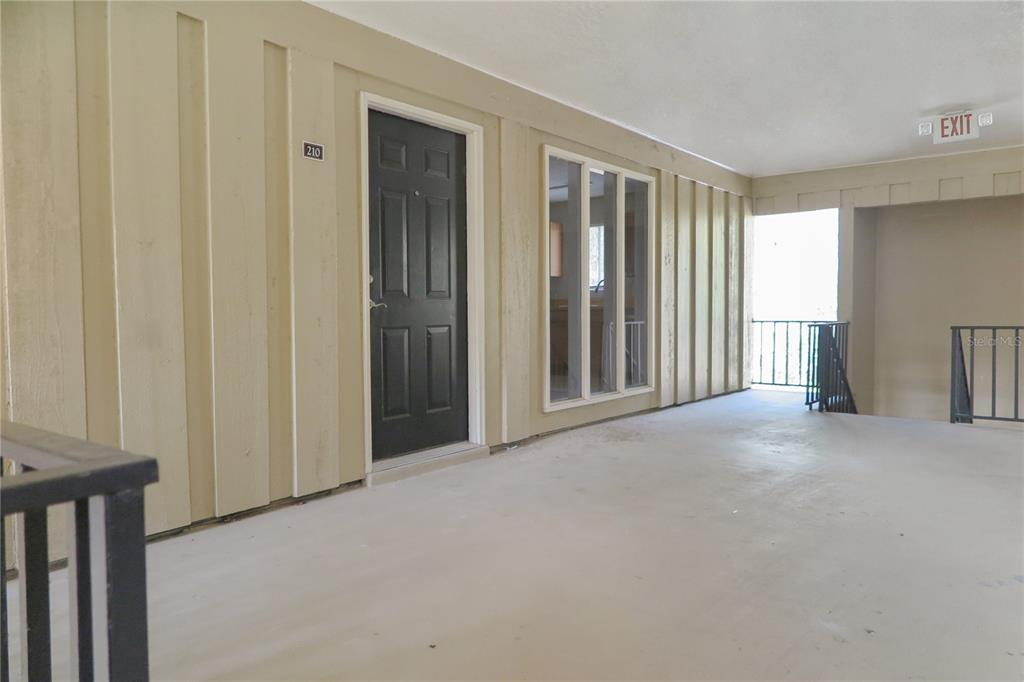 An exterior view of an apartment building hallway featuring a black door numbered 210 — 507 NW 39TH DRIVE UNIT 210, GAINESVILLE, FL