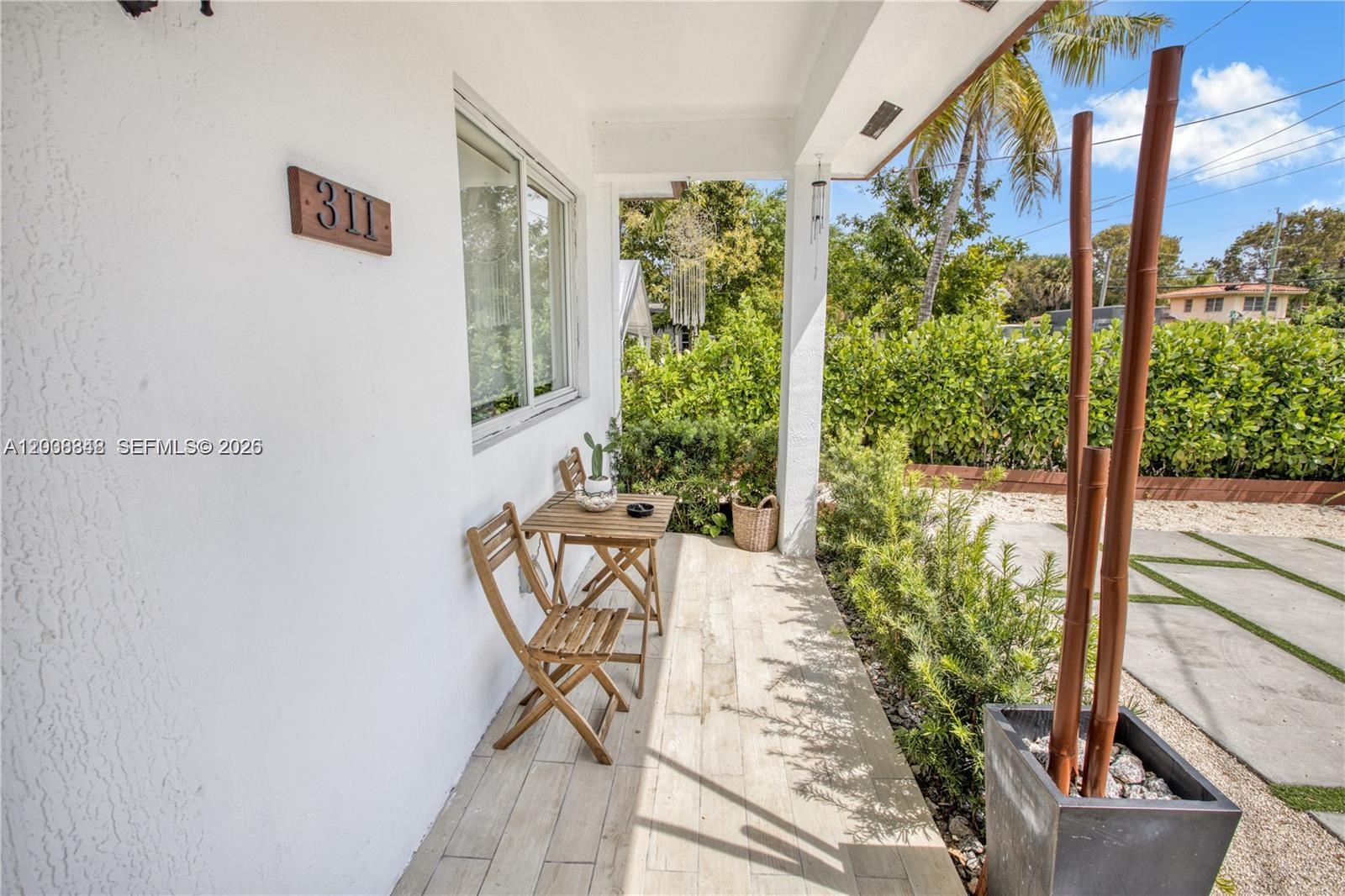 A small covered porch features a wooden bistro set, light tile flooring, and a planter — 311 NW 95th St, Miami FL 33150, MIAMI, FL