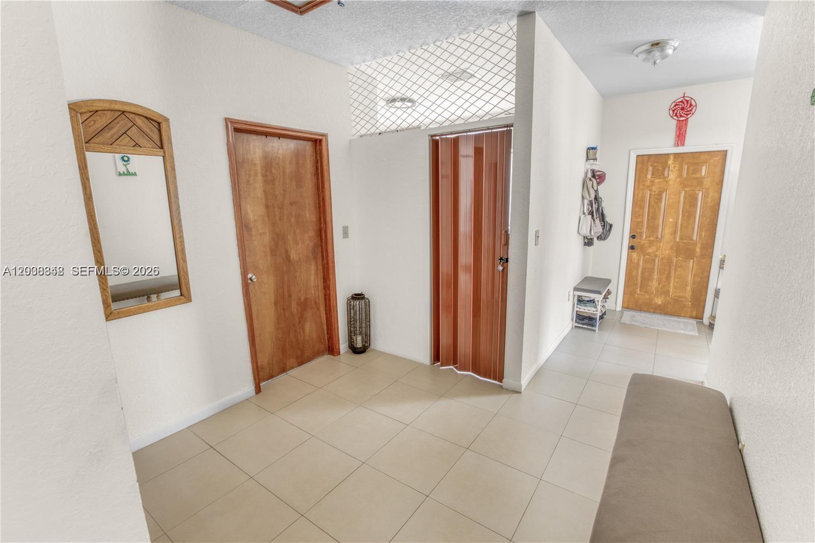 An entryway features tiled floors, a wooden door, a mirror, and a folding closet door — 311 NW 95th St, Miami FL 33150, MIAMI, FL
