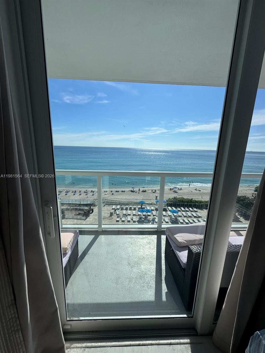 A balcony with outdoor furniture overlooks a sandy beach and the ocean — SUNNY ISLES BEACH, FL