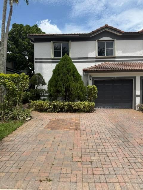 A two-story house features a paved driveway, a dark garage door, and a central evergreen tree — 2440 NW 99th Way, Sunrise FL 33322, SUNRISE, FL