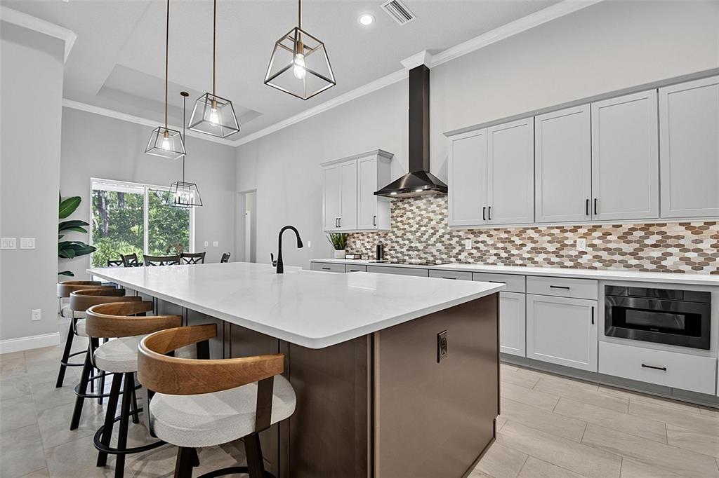 A modern kitchen features a large island with bar seating, light cabinetry, and a patterned backsplash — 23 N RIVERWALK DRIVE, PALM COAST, FL