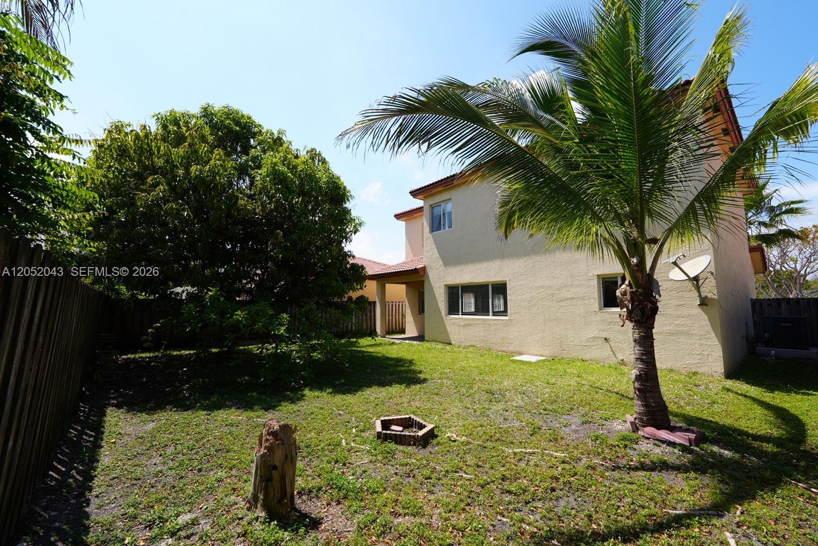 A backyard with a palm tree, a small fire pit, and a two-story stucco house — 8836 SW 221 Terr, Miami FL 33190, MIAMI, FL