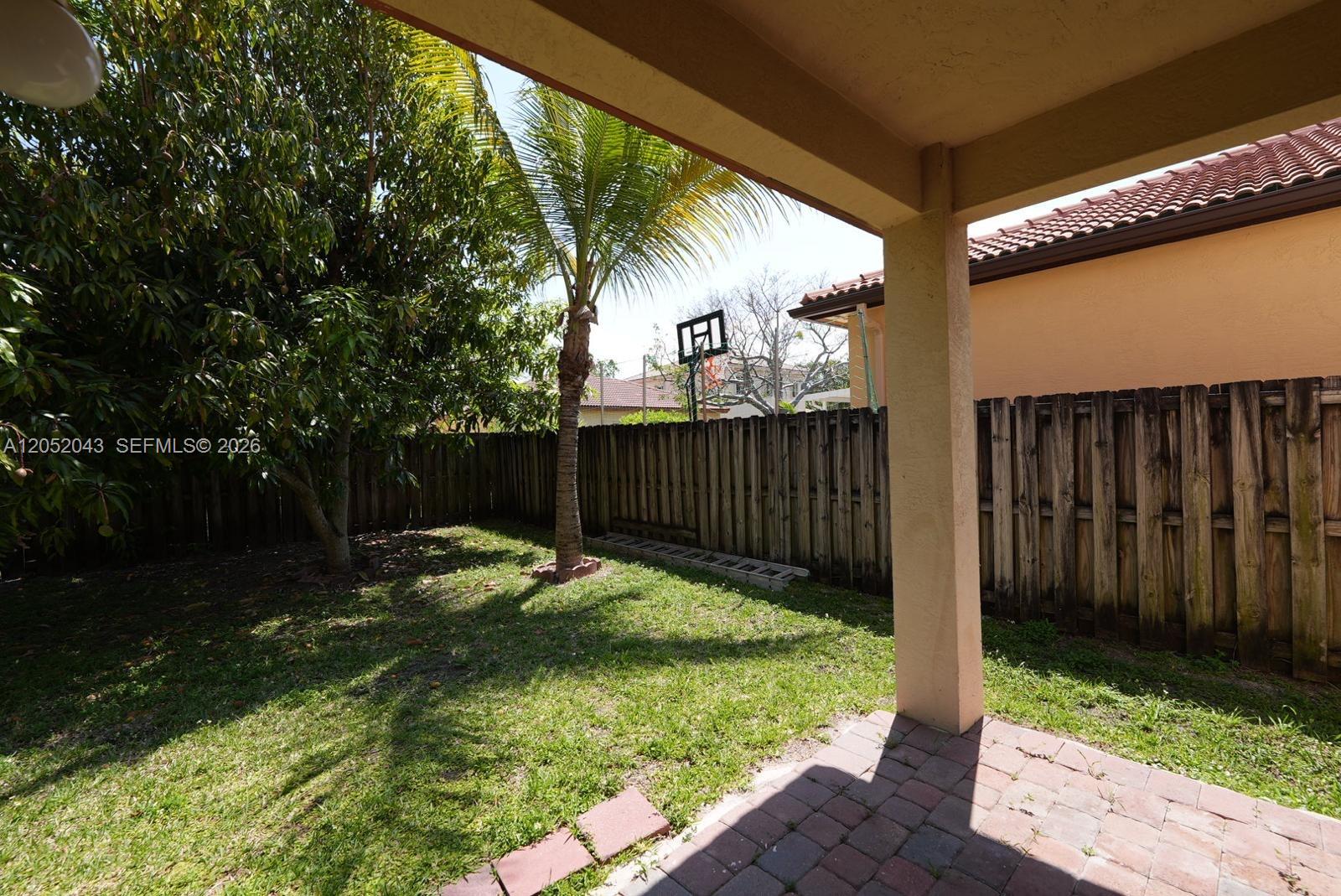 A backyard features a small patio, a palm tree, and a wooden privacy fence — 8836 SW 221 Terr, Miami FL 33190, MIAMI, FL