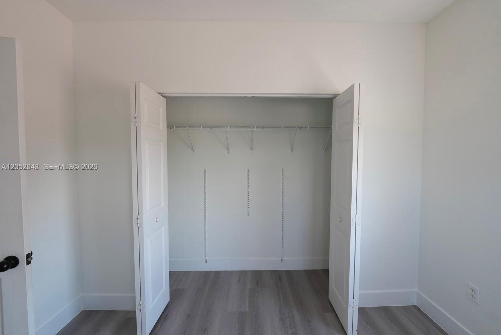 An open closet with white doors, wire shelving, and light wood-look flooring in a room — 8836 SW 221 Terr, Miami FL 33190, MIAMI, FL