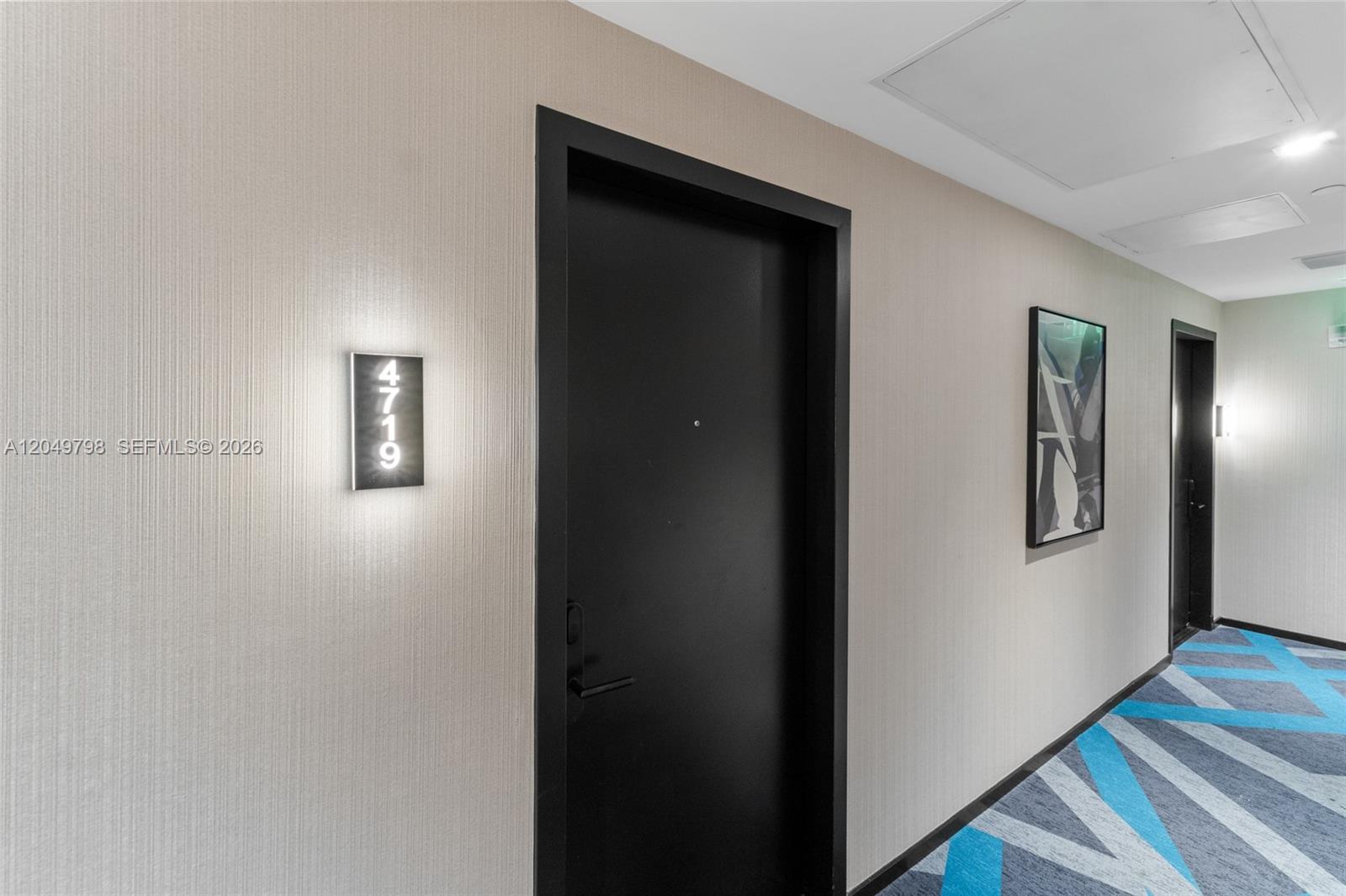 A hallway features a black door labeled 4719, textured beige walls, and patterned blue carpeting — 398 NE 5th St # 4719, Miami FL 33132, MIAMI, FL