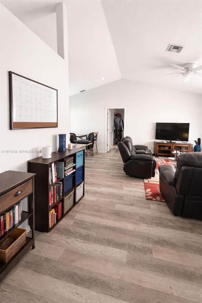 A living room features vaulted ceilings, wood-look flooring, and a dark shelving unit — 1518 SENIOR CT, Lehigh Acres FL 33971, LEHIGH ACRES, FL