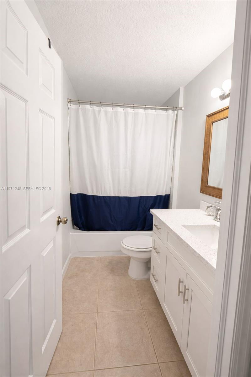 A bathroom features a white vanity, a toilet, and a shower with a blue-trimmed curtain — 1518 SENIOR CT, Lehigh Acres FL 33971, LEHIGH ACRES, FL