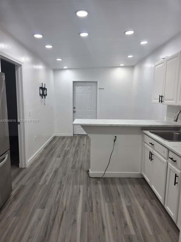 A kitchen features white cabinets, a breakfast bar, and light-colored wood-look flooring — 23 Miami Gardens Rd # 3, West Park FL 33023, WEST PARK, FL